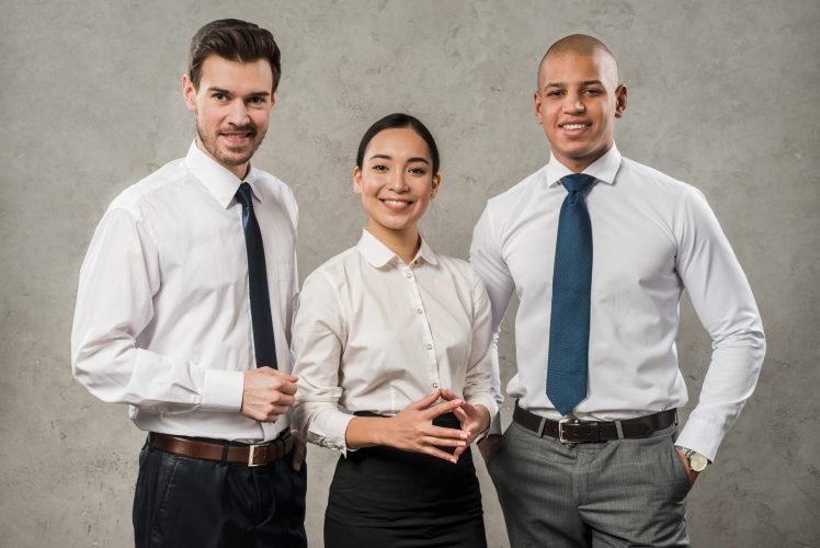 successful-young-business-partners-looking-camera-standing-against-grey-wall